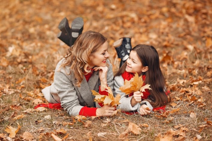 Una madre y su hija están tumbadas bocabajo, con unas hojas secas de otoño sobre un prado lleno de hojas secas de otoño