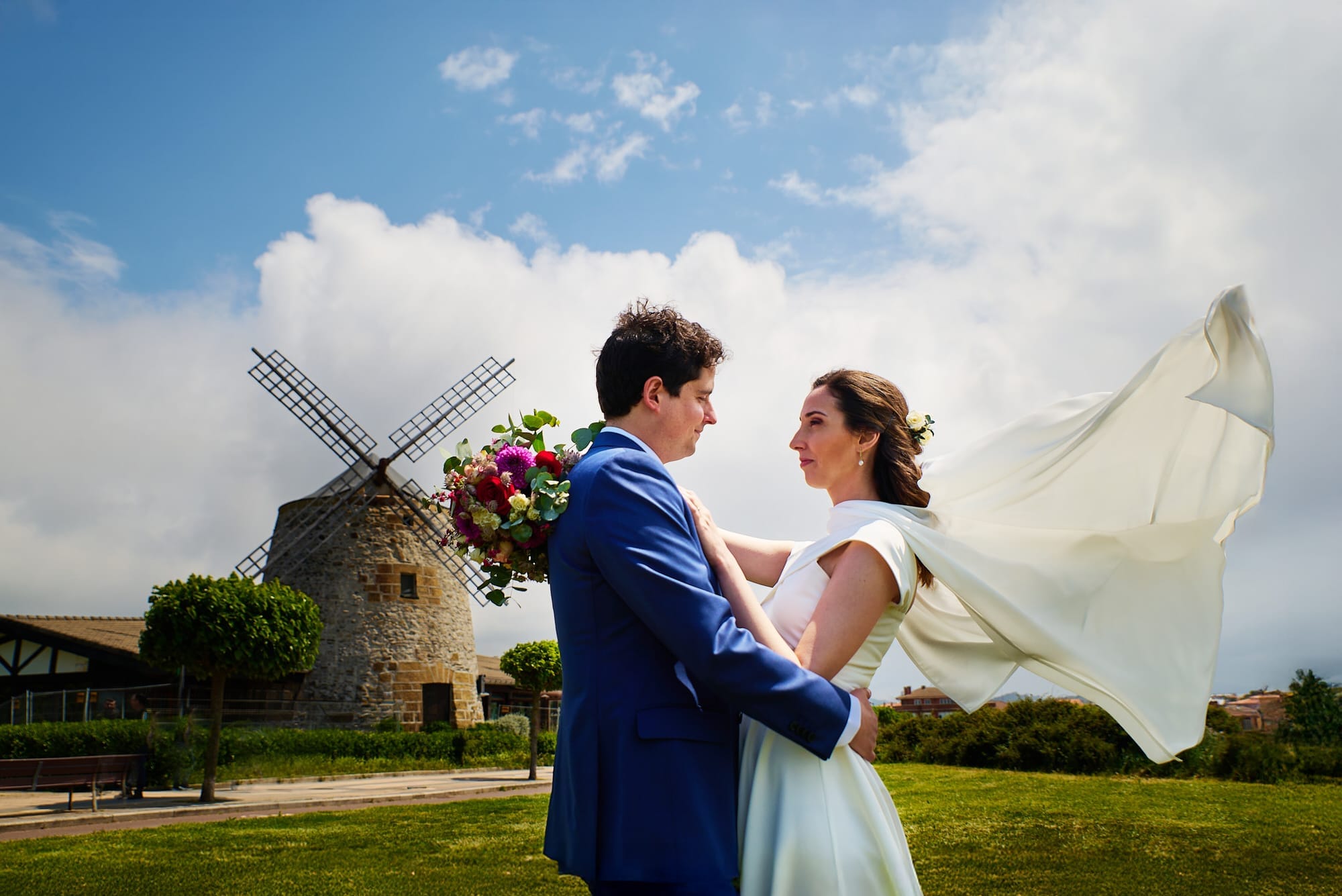 Los novios se abrazan frente al molino de Getxo en Bilbao mientras el viento levanta el velo de la novia en una espectacular pose y romántica fotografía