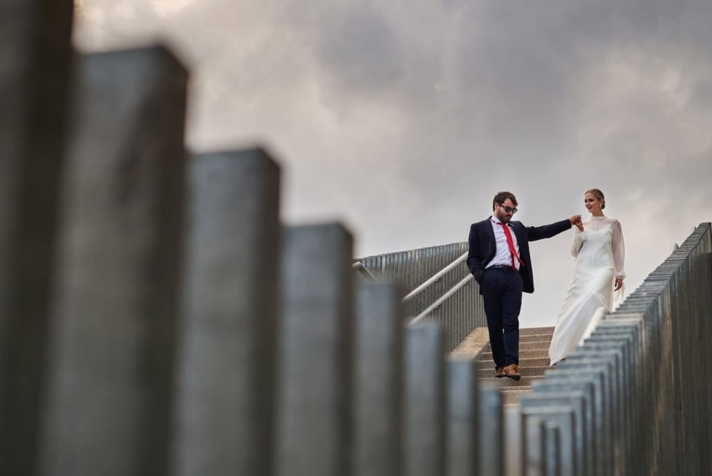 Fotos de boda unos novios al pie de unas escaleras posan para nosotros. La foto juega con líneas diagonales y perspectiva, mostrando belleza plástica