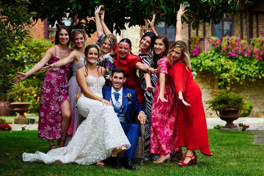 Los novios están sentados y las amigas de la novia están justo por detrás mientras posan para una foto de grupo en los Jardines de Viares