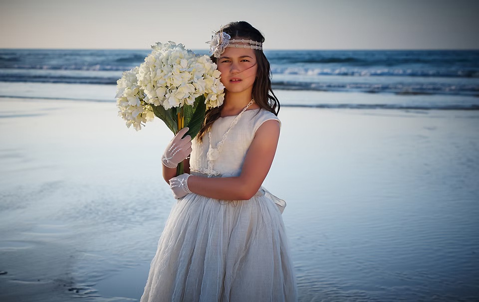 comuniones jose ferreiro 2026-12 Una niña vestida de comunión con un ramo de flores en sus manos, está posando en la playa para nosotros