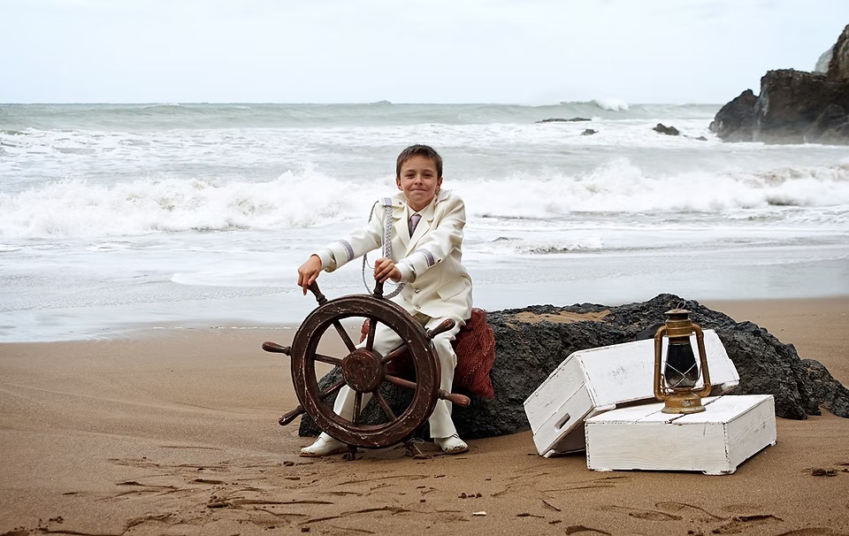 comuniones jose ferreiro 2026-15 Un niño vestido de comunión en una playa posa para nosotros con atrezzo de marinero