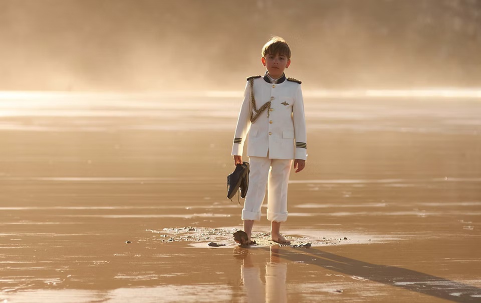 comuniones jose ferreiro 2026-8 Un niño vestido de comunión, camina por la playa en un atardecer y lleva sus zapatos en la mano y va descalzo