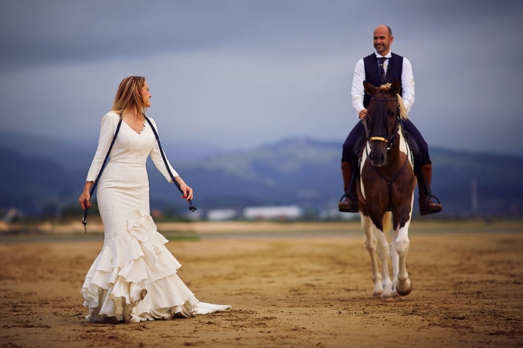 JOSE FERREIRO FOTOGRAFIA - FOTOGRAFO DE BODAS EN SANTANDER Y CANTABRIA - POSTBODA EN EL REGATON DE LAREDO la novia camina por la playa al lado de su novio , montado a caballo