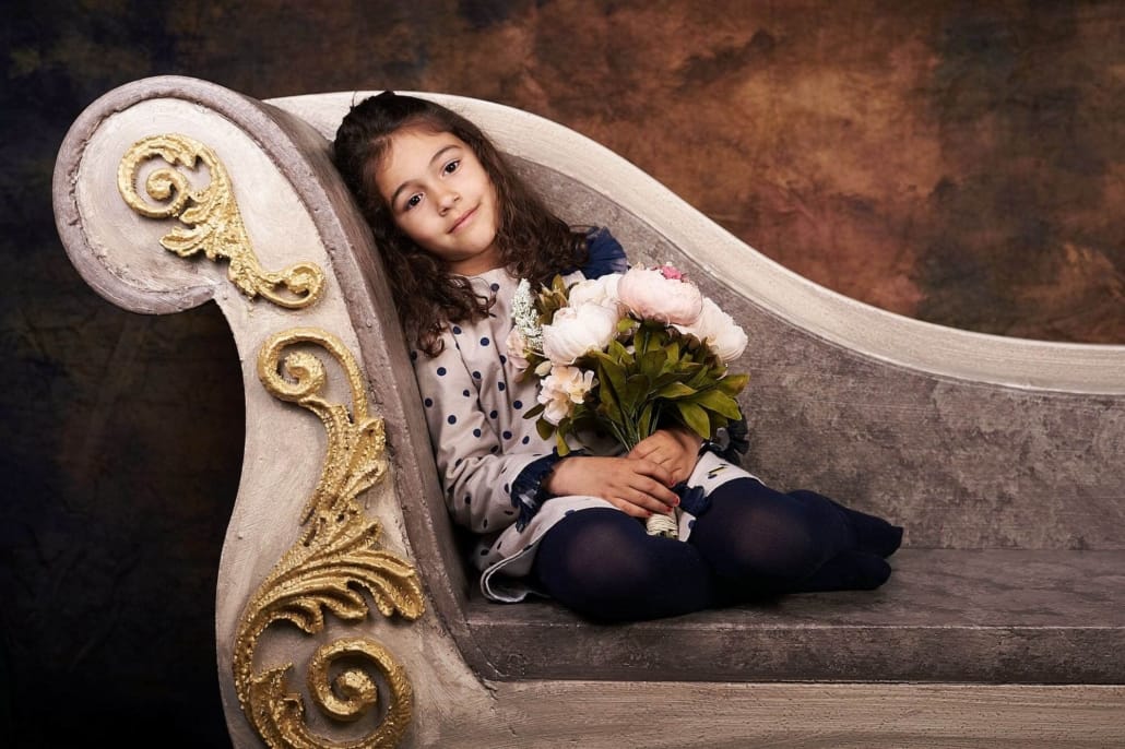 foto infantil de una niña de unos 6 años, esta posando en nuestro divan, lleva un ramo de flores