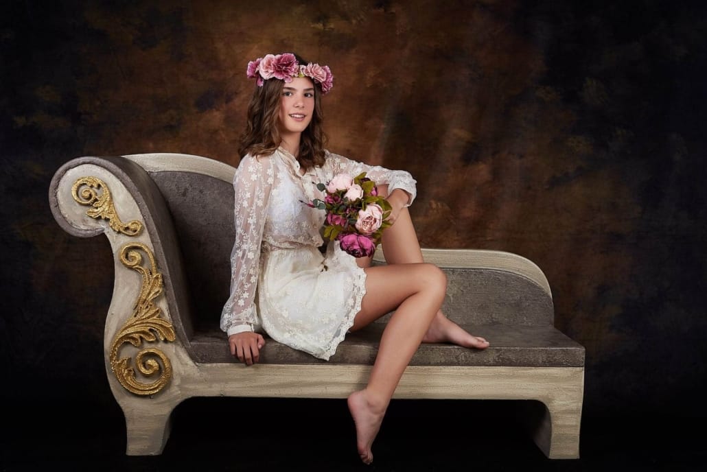 foto infantil de una niña de unos 14 años, esta posando en nuestro divan y lleva un ramo y una corona de peonias