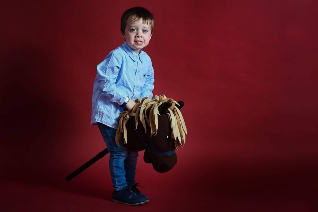 foto de estudio sobre un fondo rojo granate, el niño monta un caballo escoba