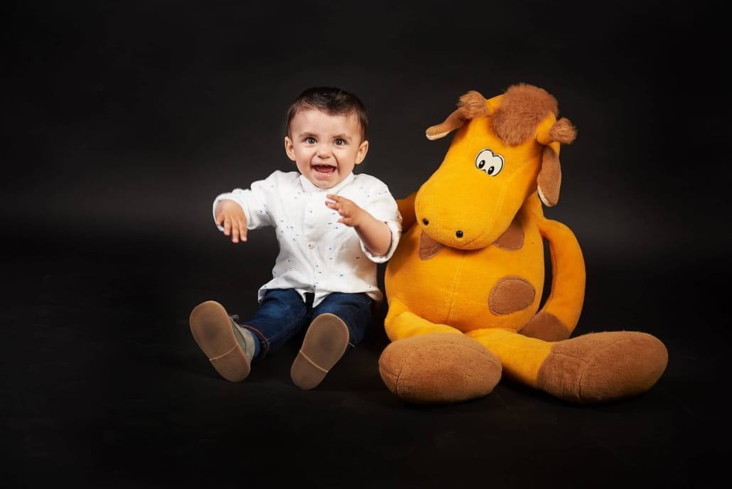 foto infantil de estudio, al niño esta al lado de un peluche gigante amarillo