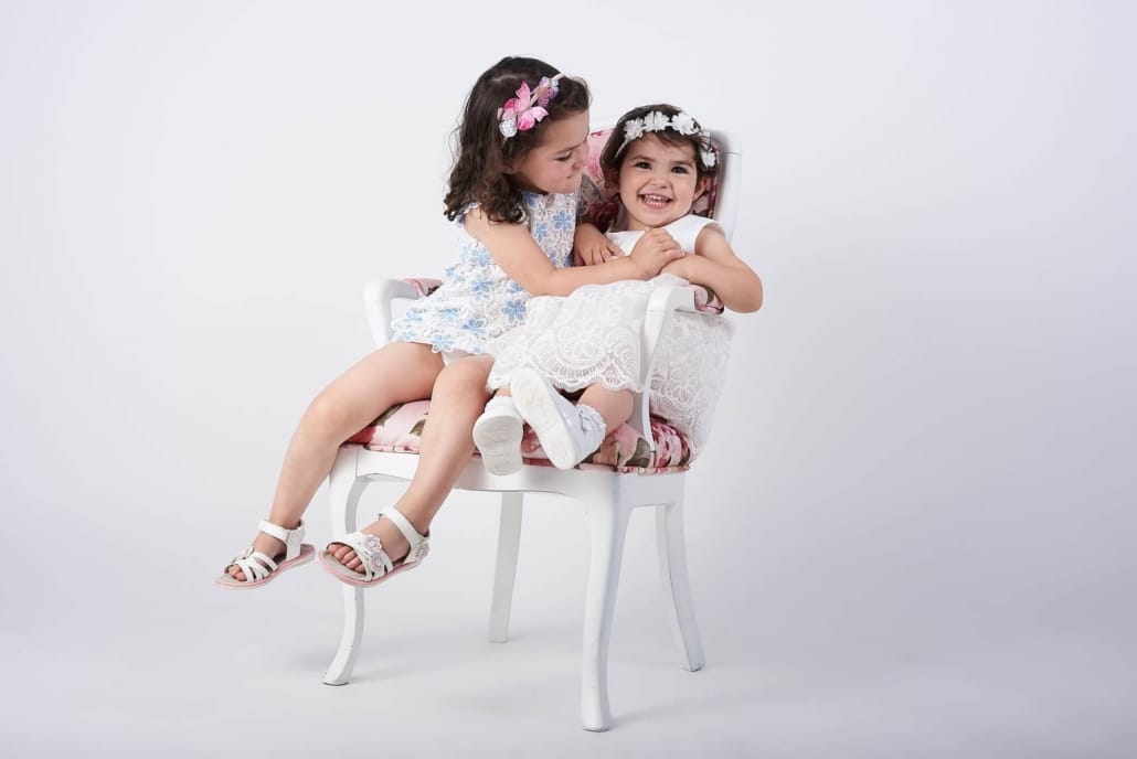 fotografia infantil en el estudio , las dos hermanas estan en una silla juntas y jugando
