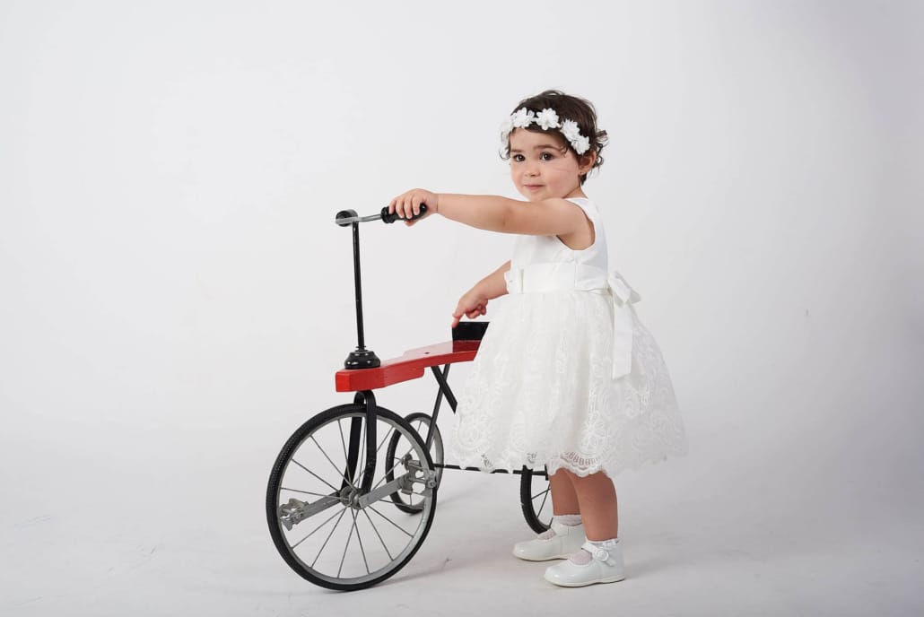 foto infantl de estudio, la niña intenta subirse a un triciclo rojo