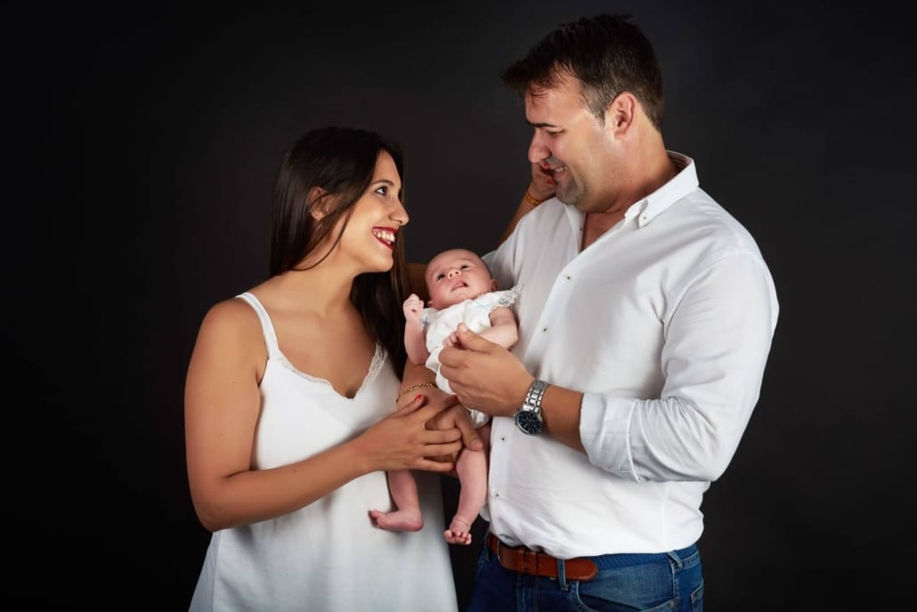 una foto familiar de una pareja con su hijo en el estudio, fondo negro , se miran y sonrien