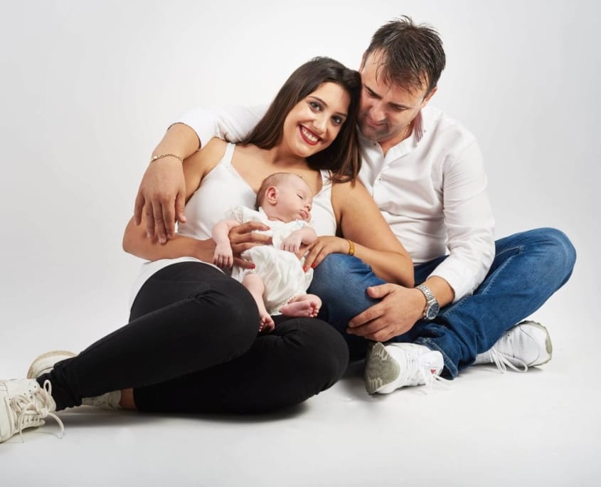 una foto familiar de una pareja con su hijo en el estudio, sentados en un fondo blanco