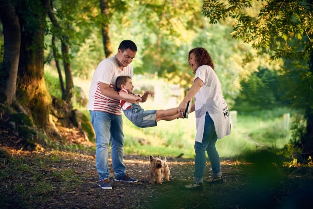 fotografia de familia, en el parque los padres sujetan al hijo y le columpian divertidamente