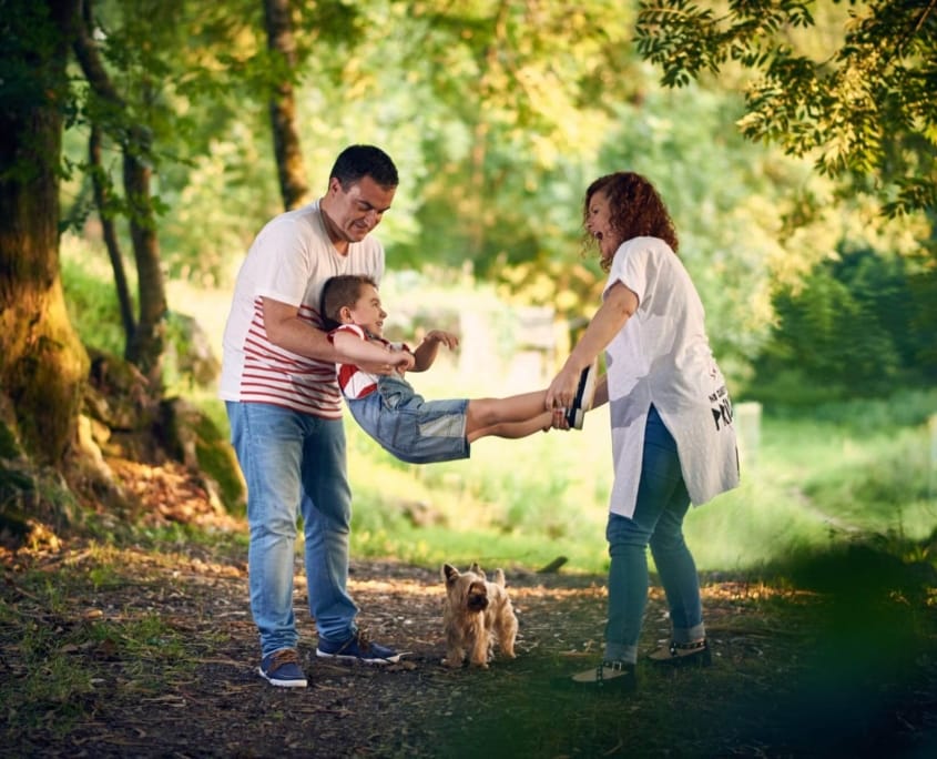 fotografia de familia, en el parque los padres sujetan al hijo y le columpian divertidamente