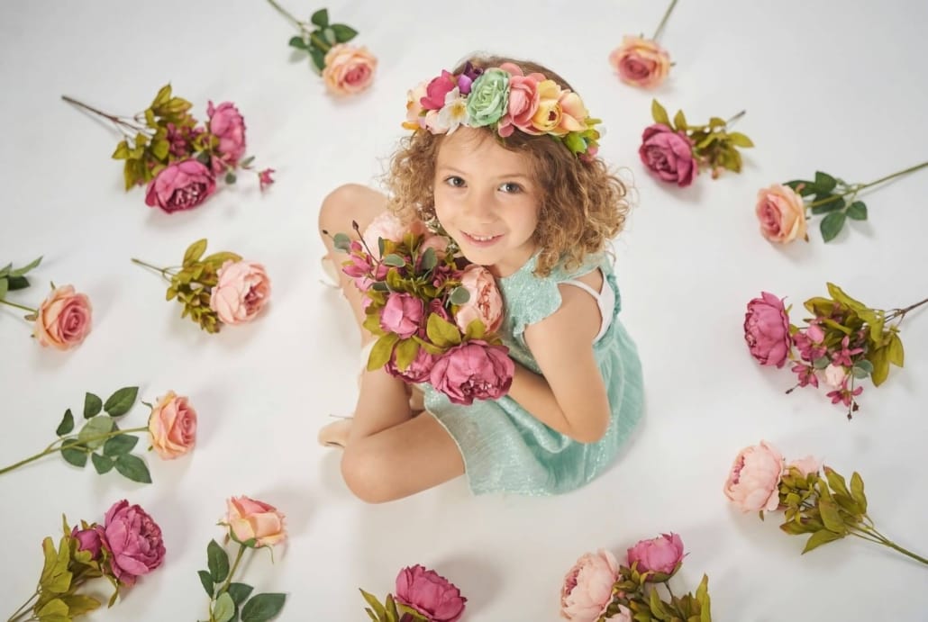 fotografia infantil en estudio, la niña esta sentada en el suelo, con fondo blanco , rodeada de flores