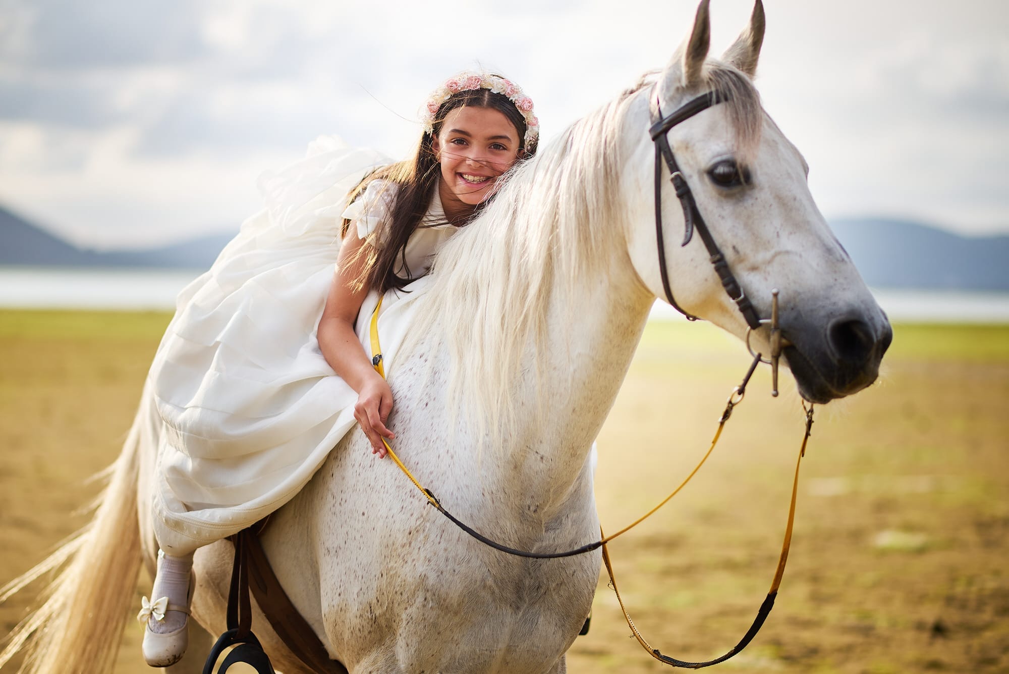 Fotografía de Comunion, en la playa del Regatón de Laredo, la niña, con su vestido de comunión monta sobre un caballo blanco y sonríe a camara