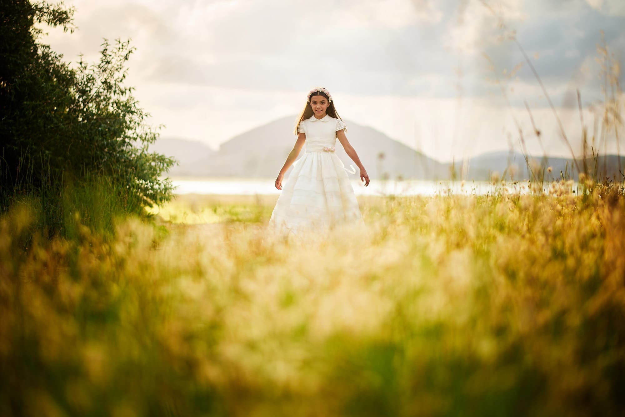 Fotografía de Comunion, a la puesta de sol en el Regatón de Laredo, la niña luce su vestido blanco en un campo de flores amarillas en un impresionante atardecer