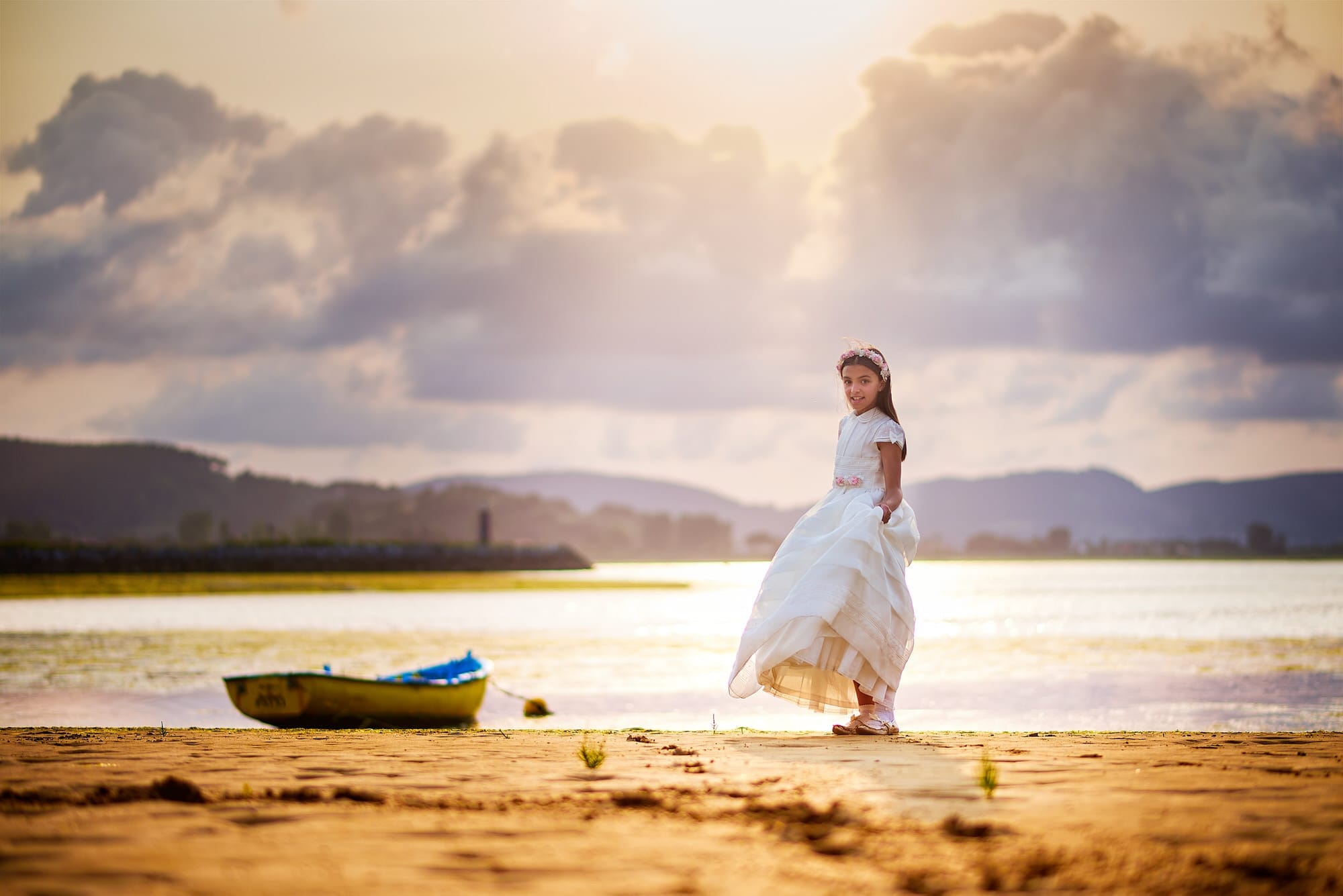 Fotografía de Comunion, al atardecer en la playa de Laredo, la niña posa junto una barca amarilla en un precioso atardecer dorado